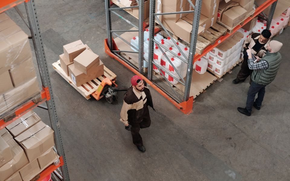 Warehouse workers coordinating stock handling beside a pallet truck